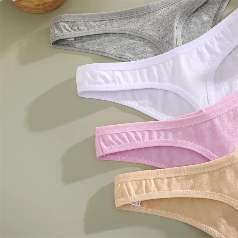 Four pairs of underwear in gray, white, pink, and beige on a light green surface.