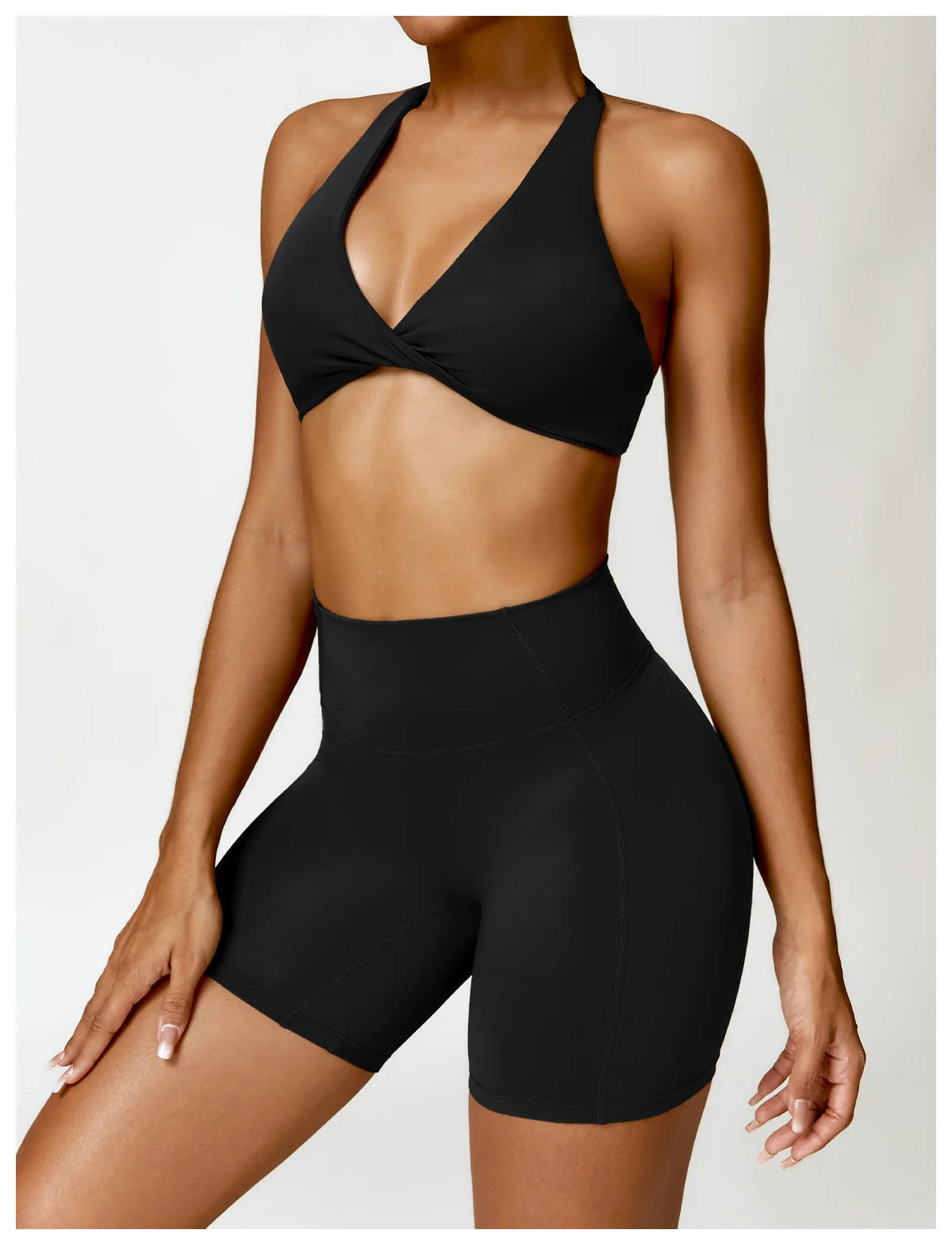 Person wearing a black sports bra and high-waisted shorts on a plain background