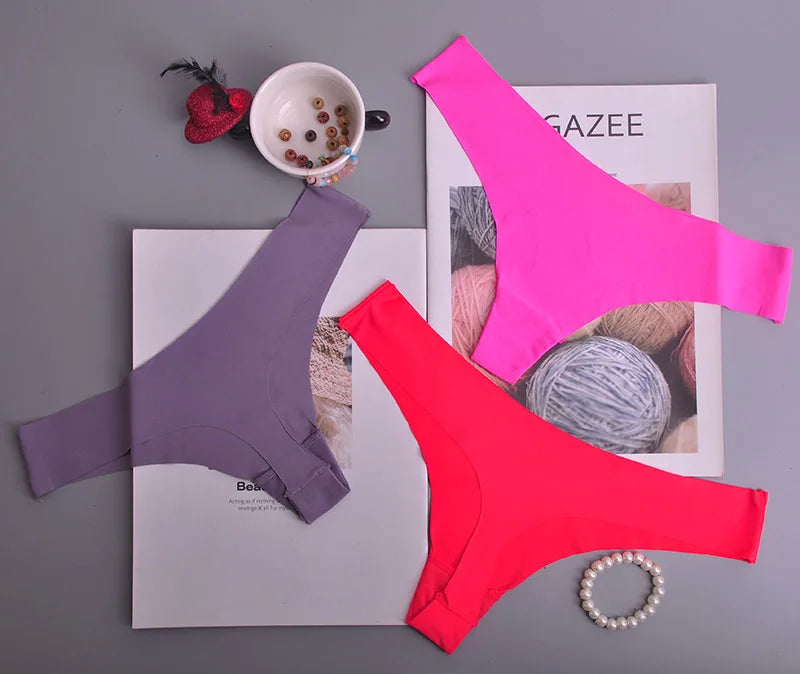 Three pairs of colorful underwear (purple, pink, red) on a magazine with a cup and yarn ball in the background.
