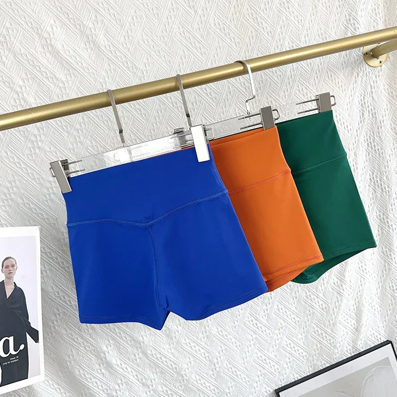 Three colorful shorts hanging on a rack against a textured white wall.
