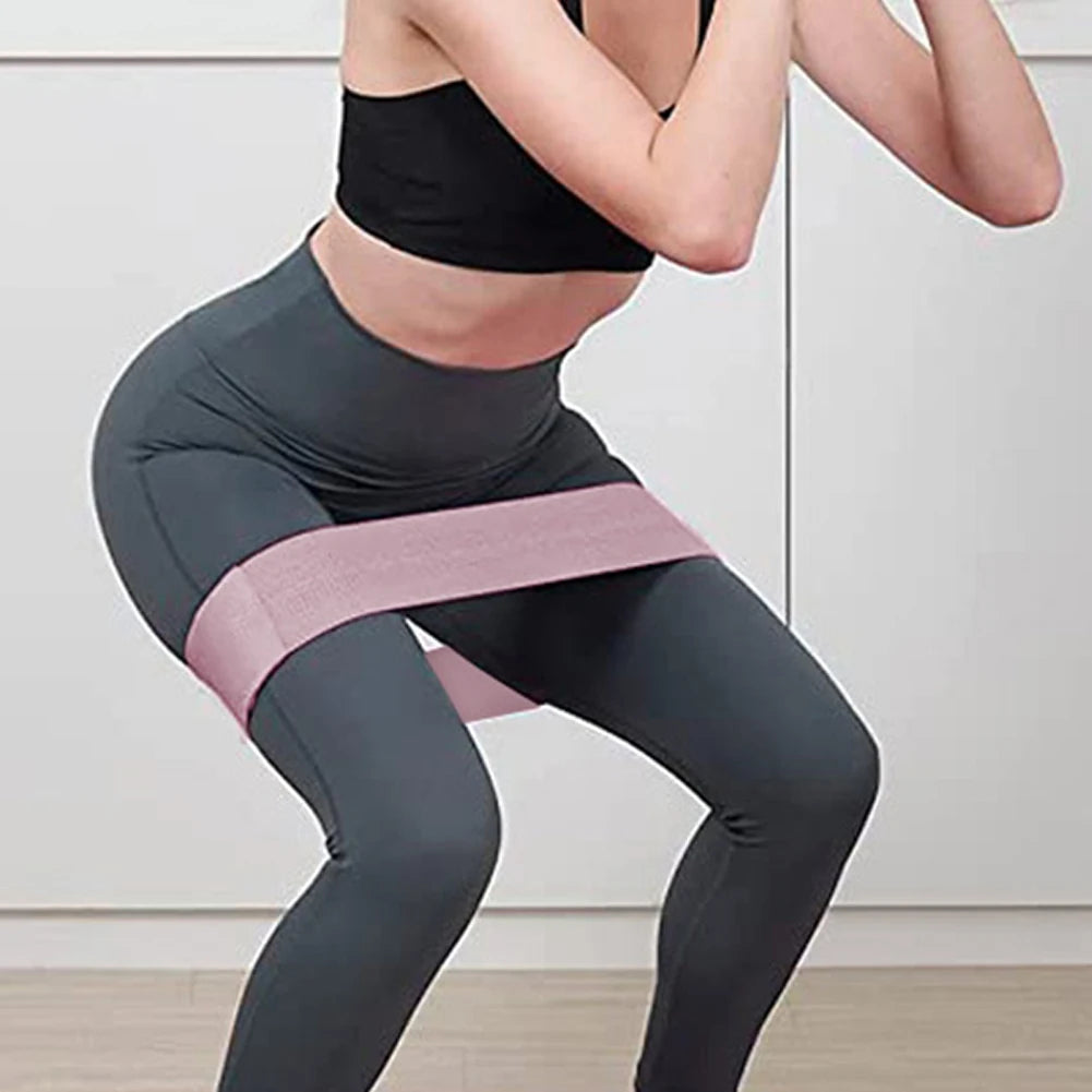 Person wearing dark gray leggings with a pink resistance band during a workout.
