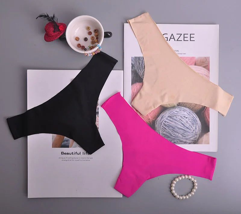 Black, pink, and beige women's underwear on a magazine with a cup and beads.